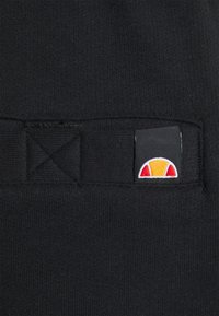Schwarzer Stoff mit einem kleinen Etikett und einem mehrfarbigen Logo, das rote, gelbe und weiße Designelemente enthält. Glatte Textur, schlichtes Design.