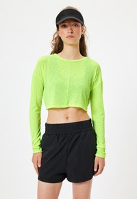 Neon grøn cropped langærmet top med tekstureret stof, parret med sorte shorts med elastisk talje. Enkel, funktionel design til træningstøj.