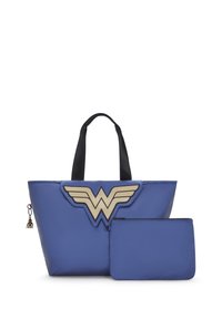 Blå toteväska med dubbla svarta handtag, prydd med en guldfärgad Wonder Woman-emblem, tillsammans med en matchande dragkedjefodral. Slät textur.