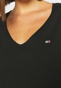 Close-up of a person wearing a black V-neck shirt with a small rectangular red, white, and blue logo on the chest area.