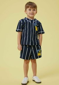 Completo corto a righe navy con camicia a bottoni che presenta una grafica di Pikachu. I pantaloni shorts hanno una vita elastica e un dettaglio coordinato di Pikachu.