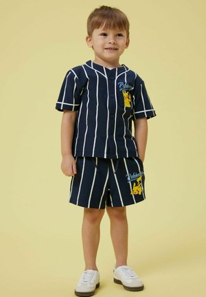 Ensemble court rayé marine avec une chemise à boutons comportant un motif de Pikachu. Le short a une taille élastique et un détail Pikachu assorti.