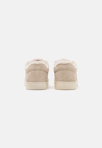Paire de baskets en daim beige avec semelles en caoutchouc blanches et doublure en peluche, vues de dos sur fond blanc.