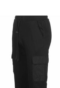 Zwarte cargobroek van zacht materiaal, met een elastische tailleband met trekkoord en een zijvak. Glad textuur, smal toelopende pasvorm.