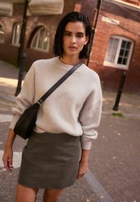 Light gray ribbed sweater with high neck, paired with a dark green corduroy mini skirt. Black crossbody bag completes the outfit.