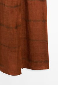 Rust-colored fabric with a subtle dark pattern runs horizontally, showing a soft texture and a side slit near the hem.