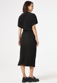 Vestido midi negro de canalé con mangas cortas, aberturas laterales y cintura ajustada. Combinado con zapatos negros gruesos y joyería sencilla.