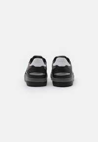Baskets noires et grises avec une texture lisse, présentant un talon rembourré, des découpes sur les côtés et un détail de logo à l'arrière.