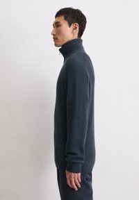 Donkerblauwe geribbelde trui met een hoge kraag en lange mouwen, voorzien van een ritskraag en een gestructureerde stof.