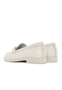 Mocassini in pelle beige con suola piatta e texturizzata e una piccola fascia anteriore. Presentano un sottile dettaglio di cucitura e un design minimalista.
