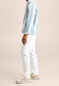 Camisa de manga larga a rayas azules y blancas, jeans blancos y zapatillas beige. La camisa presenta rayas verticales y un detalle de bolsillo.