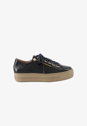 Zapatilla negra de caña baja con suela beige gruesa, cordones negros, cremallera dorada y ojales, vista lateral sobre fondo blanco.