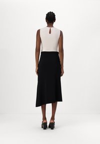 Kitsas voodriline tipp heledas beežis, millel on selja taga võtmekujuline detail. Must asümmeetriline midi-seelik sujuva tekstuuri ja elegantse langevusega.