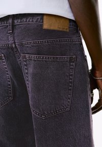 Schwarze Denim-Jeans mit einem Lederlabel von Pull&Bear auf der Rückseite. Zu den Merkmalen gehören zwei Gesäßtaschen und sichtbare Nähte.