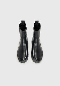 Botas de tobillo de cuero negro con acabado suave, que cuentan con una suela de goma texturizada, costuras sutiles y una cinta de tirón para un fácil calzado.