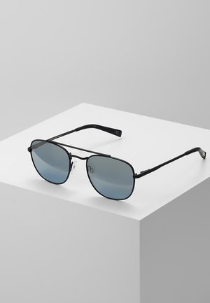 Lunettes de soleil en métal noir avec des verres ovales à teinte dégradée gris. Elles ont des branches fines et des plaquettes de nez transparentes. Placées sur une surface gris clair.