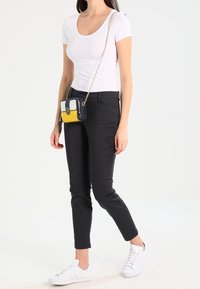 Biała koszulka z krótkim rękawem, czarne spodnie slim-fit i białe trampki. Mała torebka w żółte, czarne i białe sekcje wisi na łańcuszkowym pasku.