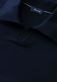 Polo de punto azul marino con cuello doblado y una etiqueta visible de la marca Façonnable en el interior del cuello.