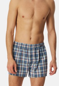 Boxer da uomo a scacchi in blu, bianco e rosso. Realizzati in tessuto leggero, presentano una vita elastica e un bottone frontale.