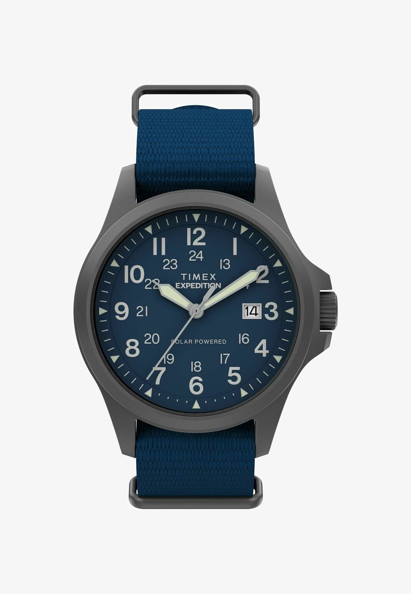 Timex Expedition ur med et mørkegråt urkasse, blå urskive, lysende tal, og et tekstureret blåt stofrem. Har datovindue ved klokken 3.