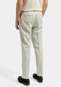 Ljusbeige byxor med avslappnad passform, elastisk midja, två bakfickor och ett strukturerat tyg, i kombination med mörkbruna skor.