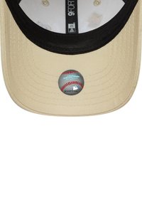 Boné de beisebol bege com a aba preta, apresentando um adesivo circular da MLB na parte inferior. O tecido tem uma textura entrelaçada.