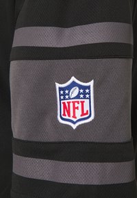 Osasto pelipaitoja NFL:lle, jossa on musta pohjaväri, harmaat raidalliset yksityiskohdat ja valkoinen brodeerattu logo punaisilla ja sinisillä yksityiskohdilla.