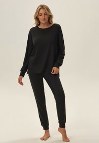 Czarny zestaw wypoczynkowy składający się z długiego rękawa topu z okrągłym dekoltem i luźnym krojem, w połączeniu z dopasowanymi spodniami. Gładka, miękka tekstura materiału.