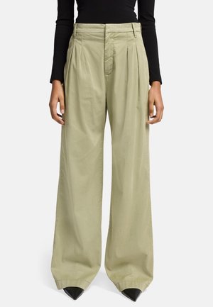 Pantaloni ampi a vita alta di colore verde chiaro, con pince, realizzati in tessuto morbido. Presentano una chiusura con zip e bottone, oltre a dettagli neri a punta.