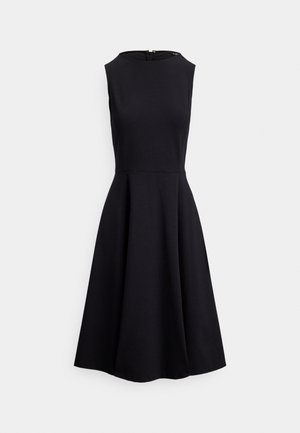 Črna obleka brez rokavov z oprijetim zgornjim delom in razširjenim krilom, izdelana iz gladkega materiala. Na zadnji strani ima diskretno zadrgo.