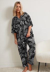 Svart pyjamas set med ett lövigt, vitt botaniskt mönster. Toppen har krage, korta ärmar, och byxorna är löst sittande med elastisk midja.