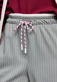 Graue Jogginghosen mit Streifenmuster und elastischem Bund, ausgestattet mit einem rosa-weißen Kordelzug und einer Seitentasche. Hergestellt aus weichem Stoff.