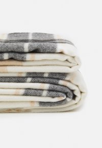Brettet rutete teppe i nyanser av grått og krem, med en myk tekstur og ferskenfargede aksenter samt et vevd design, laget av et varmt materiale.