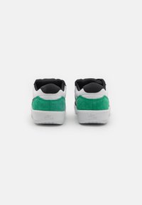 A Nike cipők fekete textil felsőrésze zöld velúr sarkakkal és fehér gumitalppal rendelkeznek, amelyen logórészlet található a hátoldalon.