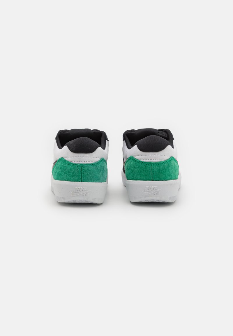 Les chaussures Nike présentent une tige en textile noire, des accents de talon en daim vert et une semelle en caoutchouc blanche avec un détail du logo à l'arrière.