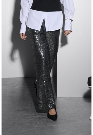 Conjunto en blanco y negro que presenta un chaleco negro ajustado sobre una camisa blanca suelta, combinado con pantalones de lentejuelas plateadas brillantes hasta el suelo y tacones negros.