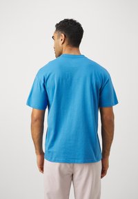 T-skjorte med kort erme i turkis bomull. Rund hals og rett snitt. Jevn tekstur med et minimalistisk design, uten synlige logoer eller mønstre.