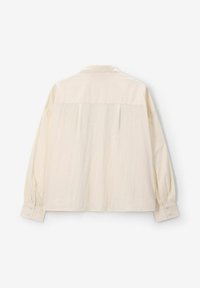 Beige long-sleeve shirt with a buttoned cuff, a relaxed fit, and a pleated back design. Light, textured fabric with a soft appearance.