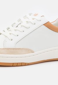 Sneaker bianca in pelle con dettagli color talpa, sovrapposizione in suede testurizzato e lacci piatti bianchi. Presenta una suola in gomma con scanalature orizzontali.