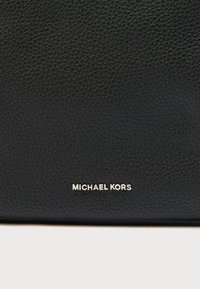 Μαύρη δερμάτινη τσάντα με υφή στην επιφάνεια και εμφανές ασημί λογότυπο "MICHAEL KORS". Καθαρές γραμμές και μίνιμαλ σχεδιασμός.