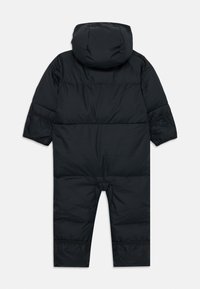 Combinaison de neige noire avec capuche, présentant des poignets élastiques, une texture lisse et des panneaux de conception segmentés. Convient pour les vêtements par temps froid.