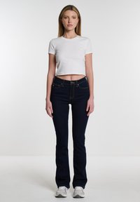 Camiseta blanca corta y pantalones vaqueros acampanados de color azul oscuro con costuras en contraste, que cuentan con bolsillos en la parte delantera y una cintura ajustada.