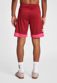 Mörkröda sportshorts med en rosa texturerad fåll, elastisk midja och logotypdetalj. Tyget verkar lätt och andningsbart.