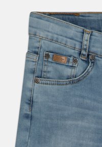 Jean in denim blu chiaro con una texture liscia, dotati di una piccola tasca frontale, rivetti in ottone e una patch in pelle del brand sulla vita.