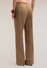 Pantaloni a gamba larga in lino khaki, con vita alta, dettagli sulla cucitura posteriore e una leggera lucentezza. Abbinati a bracciali in legno sul polso.