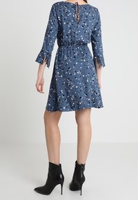 Sininen mekko, jossa on kukkakuvio, joustava vyötärö ja levenevät hihat. Yhdistetty mustiin nilkkureihin, joissa on hopeiset niitit.