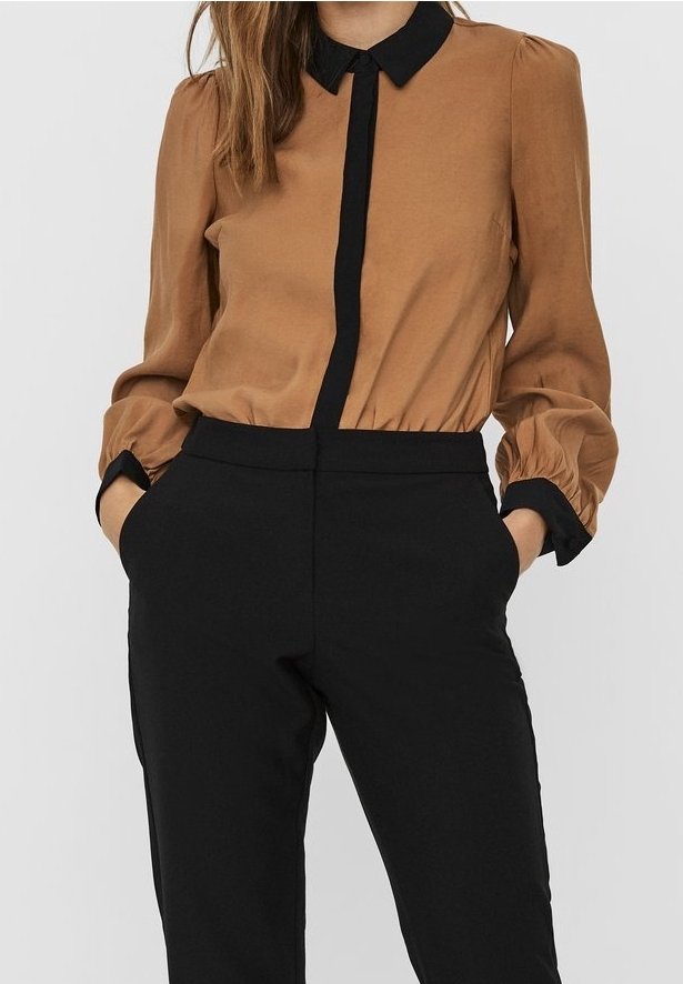 Blusa marrone con colletto e placca neri, maniche elastiche; abbinata a pantaloni neri su misura con tasche laterali.