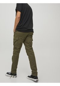 Spodnie bojówki w oliwkowej zieleni z licznymi bocznymi kieszeniami, zwężanym krojem i lekkim materiałem. Połączone z czarnymi trampkami z płótna.