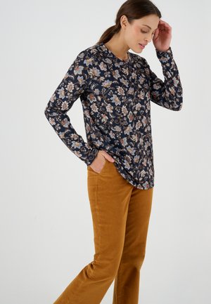 Top lungo a maniche lunghe con motivo floreale in navy, con scollatura rotonda, abbinato a pantaloni in corduroy color senape. Tessuto strutturato, silhouette aderente.