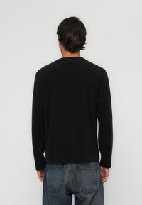 Langermet svart skjorte laget av myk stoff, med rund hals og avslappet passform, kombinert med falmede blå jeans.